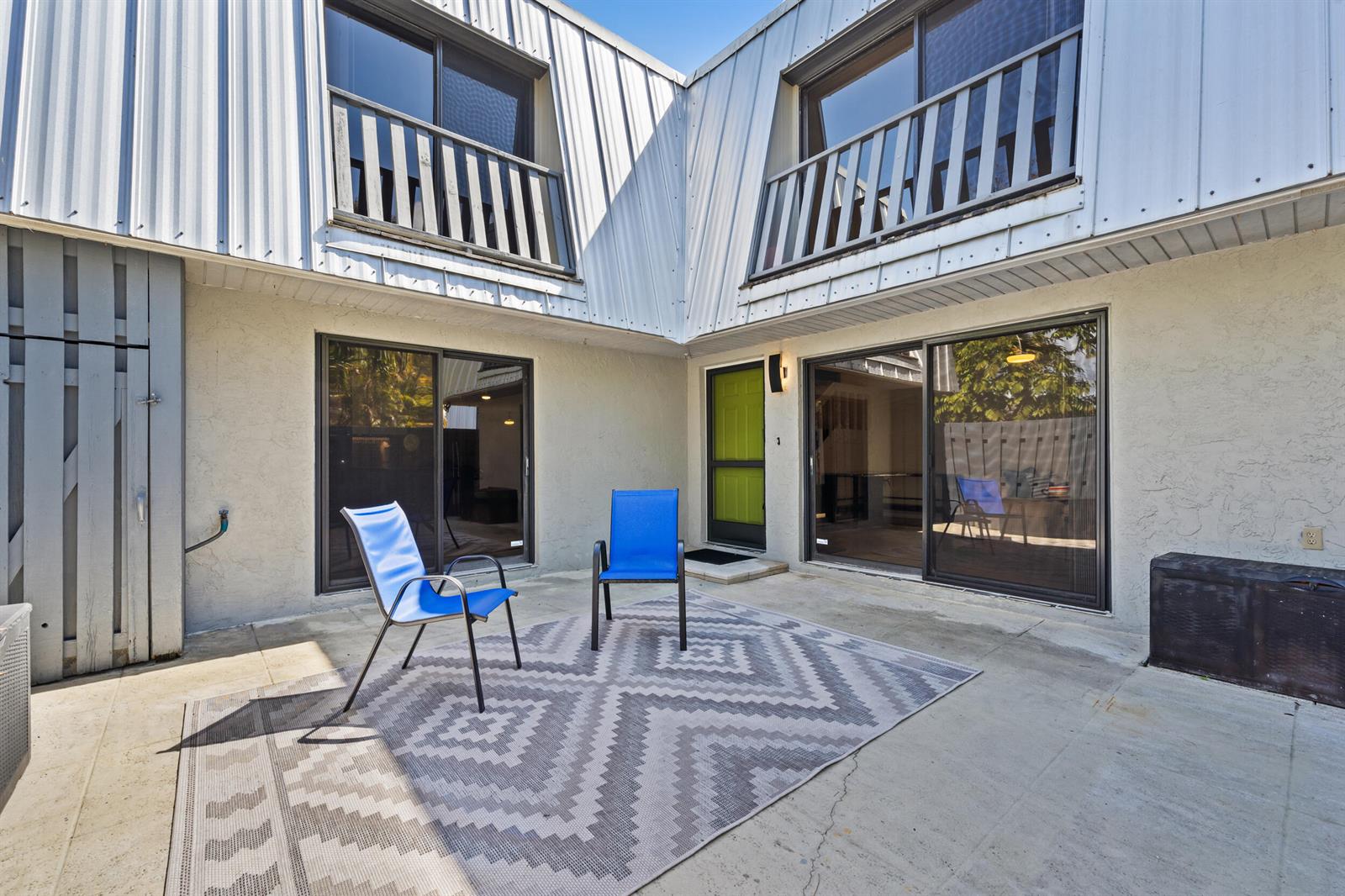 A concrete patio features two blue chairs on a patterned rug outside a two-story building — 3852 SE Jefferson Street, Stuart FL 34997, STUART, FL