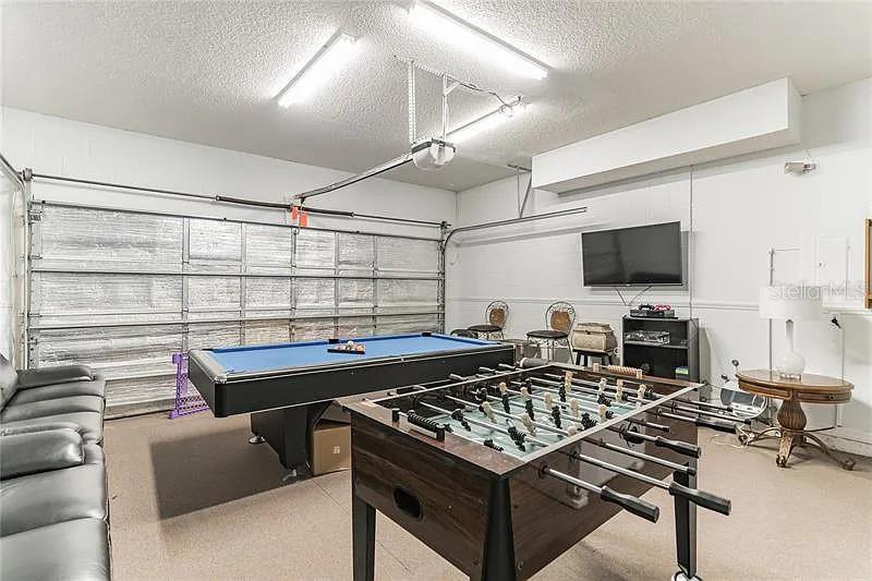 This garage is furnished as a game room with a pool table and a foosball table — 8452 SECRET KEY COVE, KISSIMMEE, FL