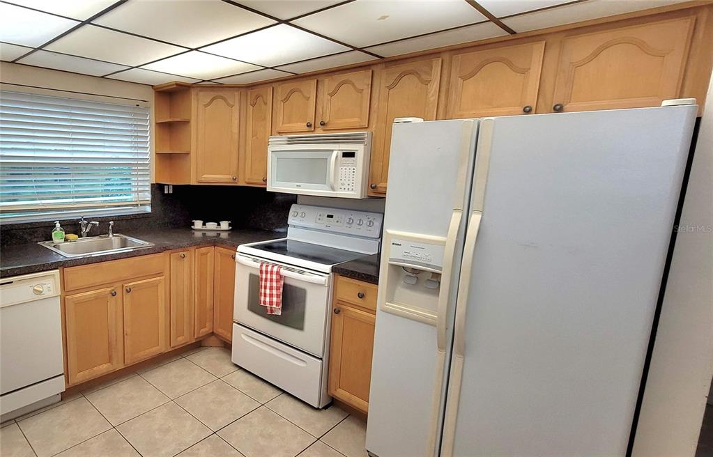 A kitchen features light wood cabinets, white appliances, a tiled floor, and a drop ceiling — 9861 Sunrise Lakes  Blvd SUNRISE LAKES BOULEVARD UNIT 310, SUNRISE, FL