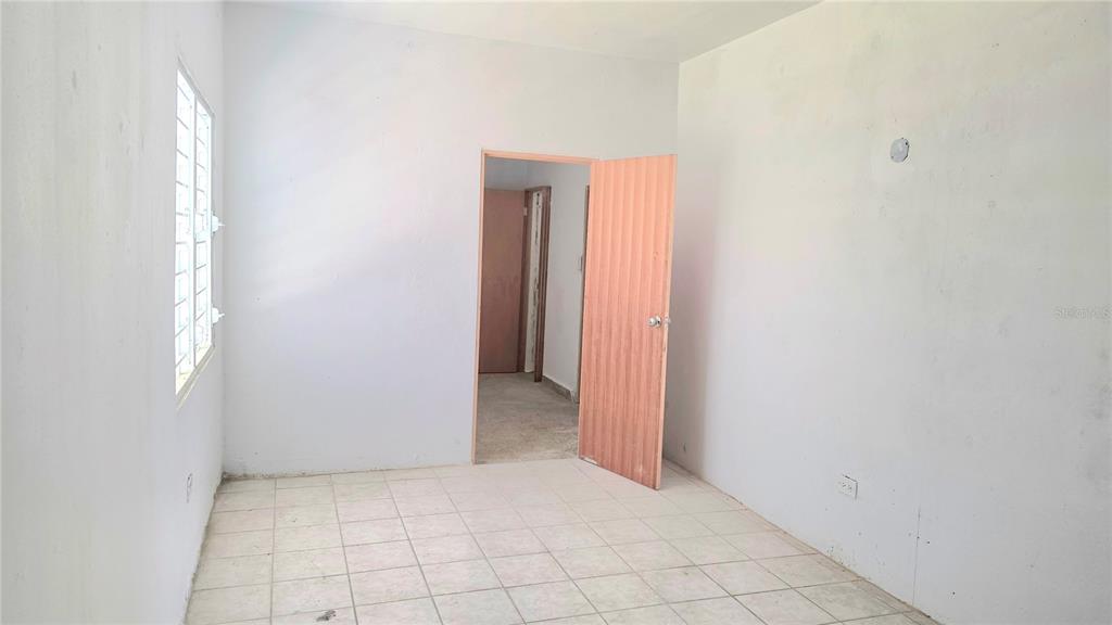An empty room with white walls, tiled flooring, a window, and an open wooden door — Bloque AB  5 CALLE JULIO ANDINO, SAN JUAN, PR