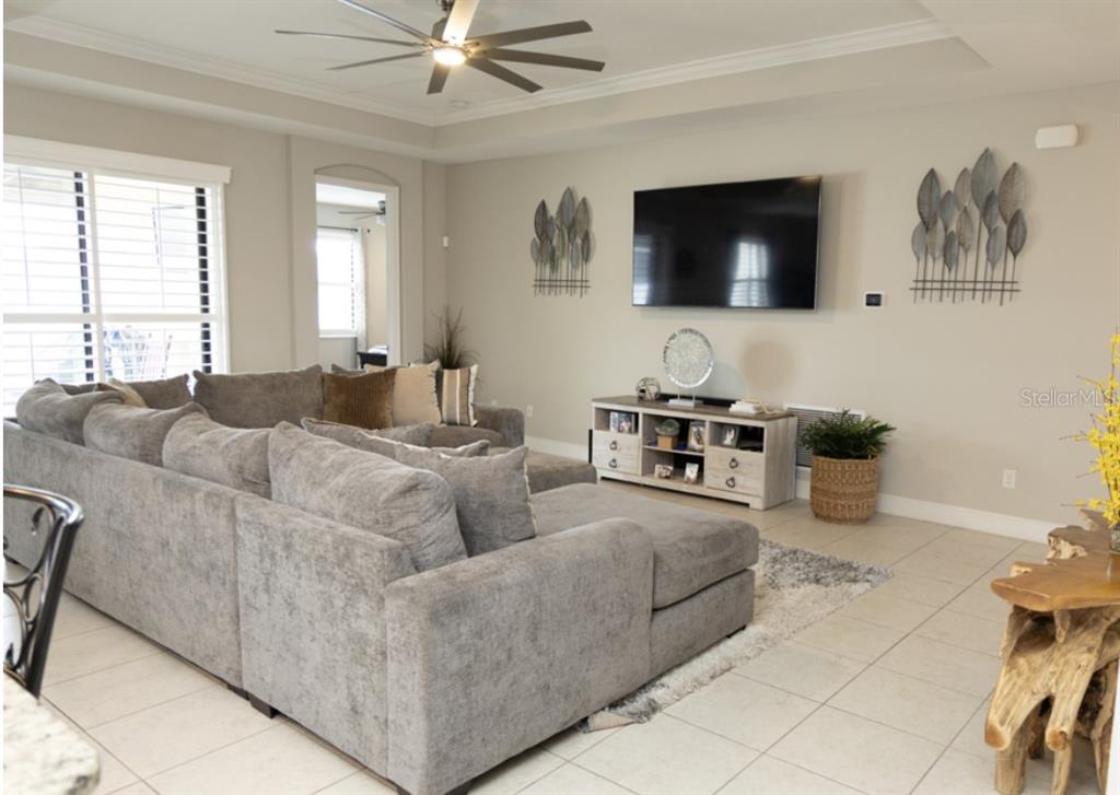 A living room features a large gray sectional sofa, a wall-mounted television, and tile flooring — 1216 OLD WINDSOR WAY, SPRING HILL, FL