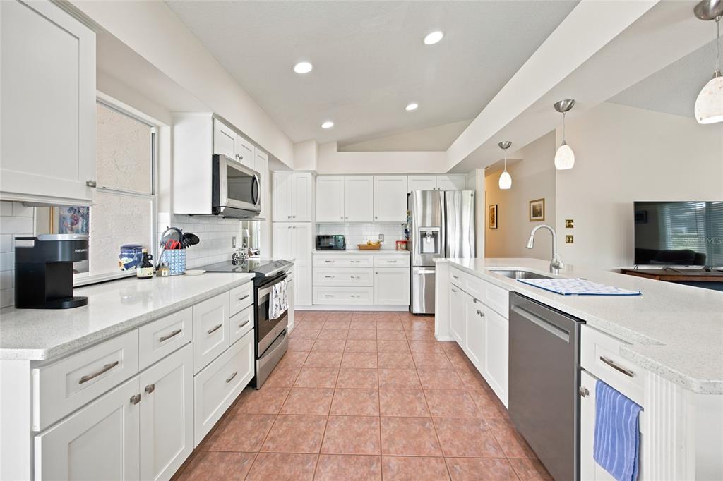 A bright kitchen features white cabinets, stainless steel appliances, quartz countertops, and tiled flooring — 2292 WHISPER WALK DRIVE, SPRING HILL, FL