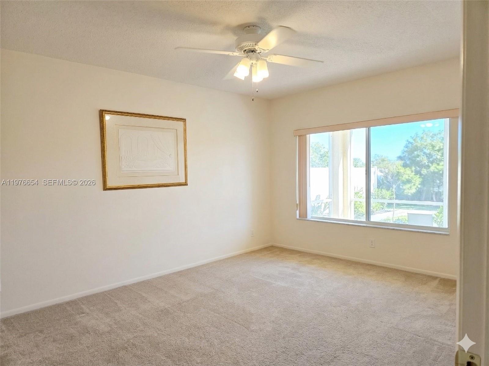 A bedroom features beige carpeting, off-white walls, a ceiling fan, and a large window — 330 SE 2nd St # 403H, Hallandale Beach FL 33009, HALLANDALE BEACH, FL