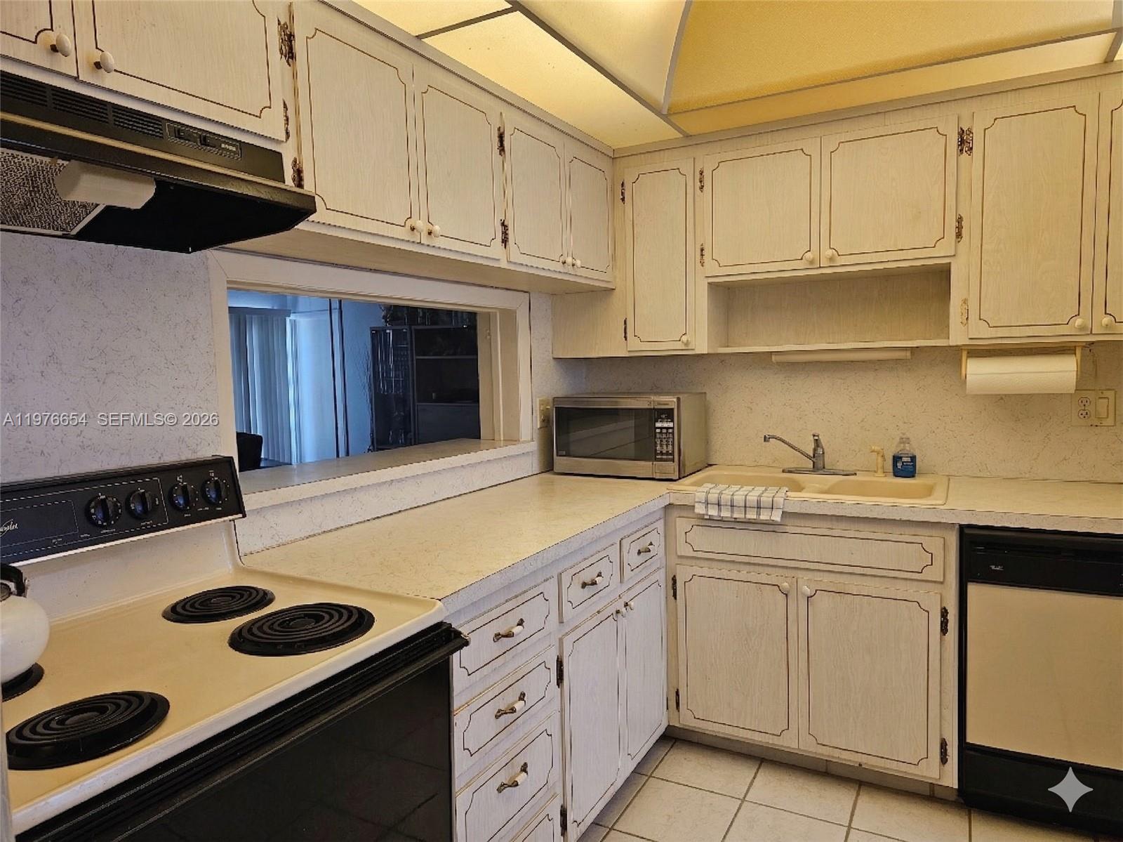A kitchen features white wood-grain cabinets, a black stove, a microwave, and a double sink — 330 SE 2nd St # 403H, Hallandale Beach FL 33009, HALLANDALE BEACH, FL