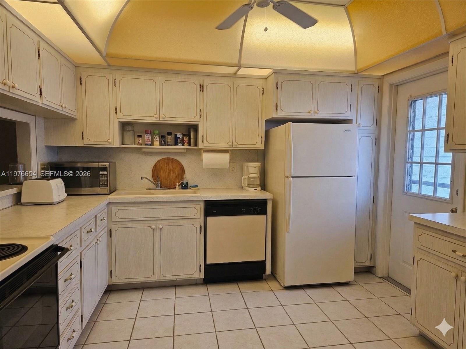 A kitchen features white cabinets, white appliances, a tiled floor, and a vaulted ceiling — 330 SE 2nd St # 403H, Hallandale Beach FL 33009, HALLANDALE BEACH, FL