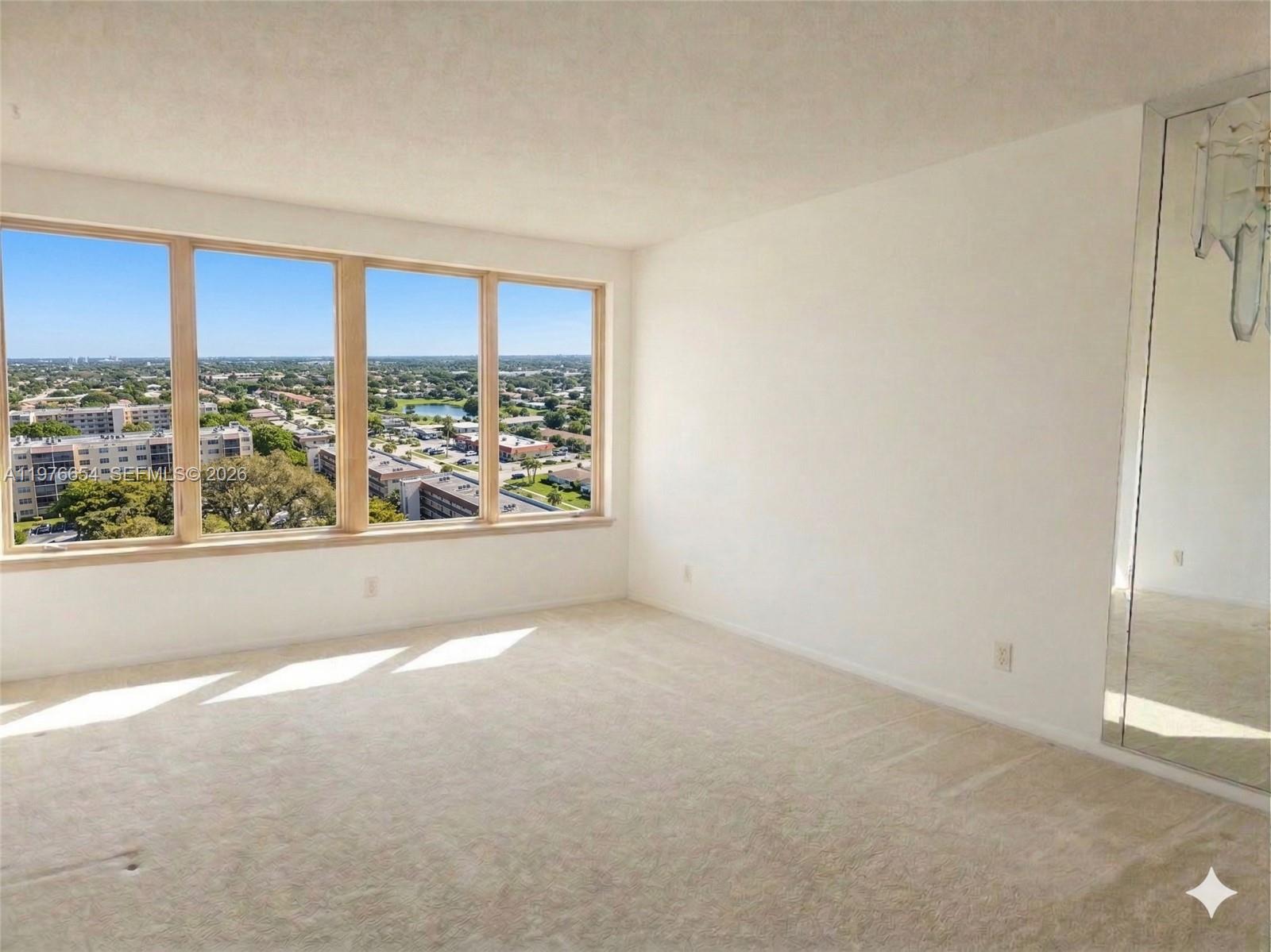 An empty room with beige carpeting, white walls, and a large window overlooking a neighborhood — 330 SE 2nd St # 403H, Hallandale Beach FL 33009, HALLANDALE BEACH, FL