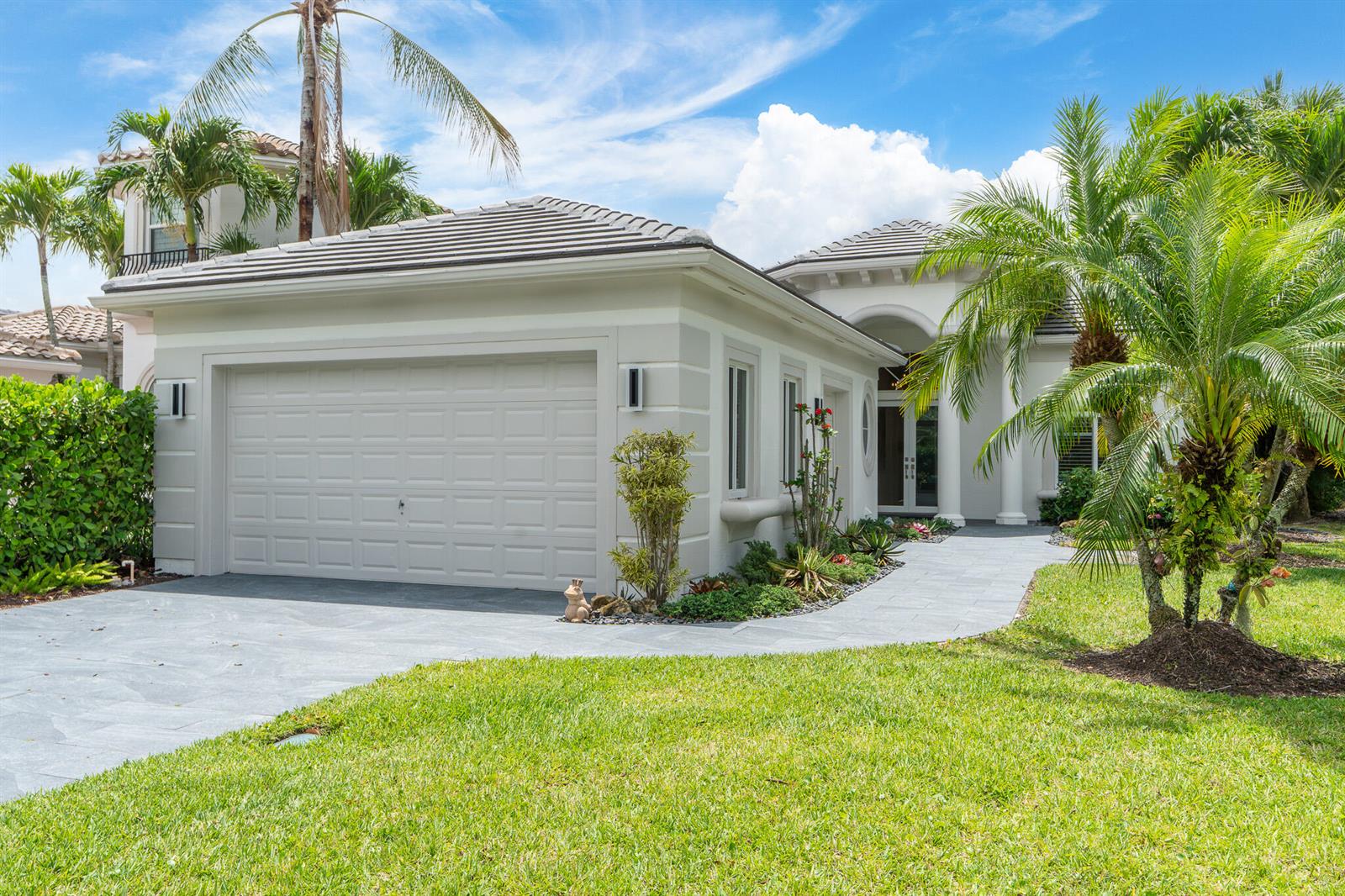 A light-colored house with a two-car garage, a stone walkway, and surrounding palm trees — 7916 Montecito Place, Delray Beach FL 33446, DELRAY BEACH, FL