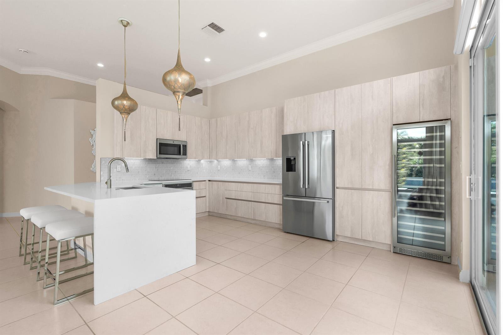 A modern kitchen features light wood cabinetry, stainless steel appliances, and a white waterfall island — 7916 Montecito Place, Delray Beach FL 33446, DELRAY BEACH, FL
