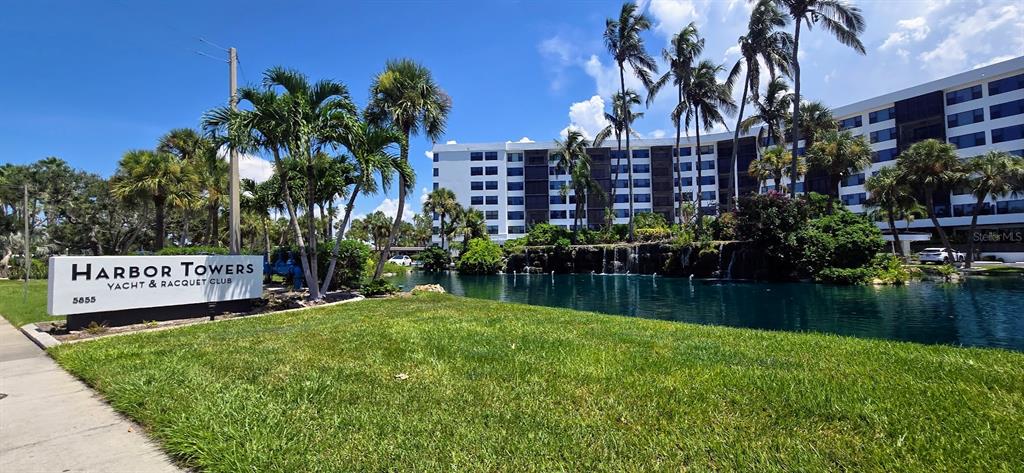 A sign for Harbor Towers Yacht & Racquet Club stands before a pond and building — 5855 MIDNIGHT PASS ROAD UNIT 314, SARASOTA, FL