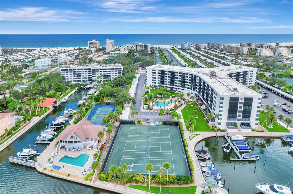 An aerial view shows a waterfront condominium complex with tennis courts, swimming pools, and boat slips — 5855 MIDNIGHT PASS ROAD UNIT 314, SARASOTA, FL