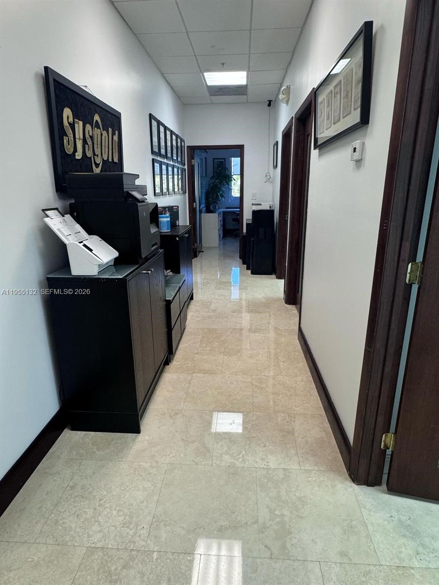 A narrow office hallway features tile flooring, dark wood cabinets, and several framed wall decorations — 7791 NW 46th St # 219, Doral FL 33166, DORAL, FL