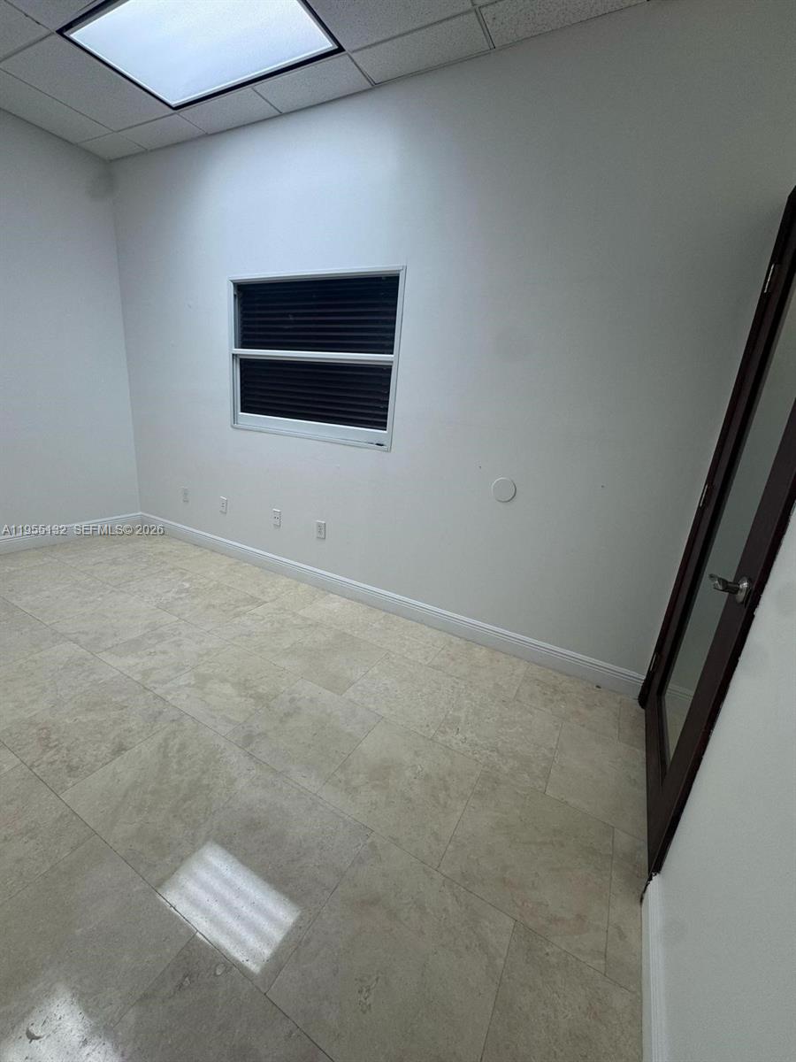 An empty office space features light-colored tile flooring, white walls, and a single window — 7791 NW 46th St # 219, Doral FL 33166, DORAL, FL