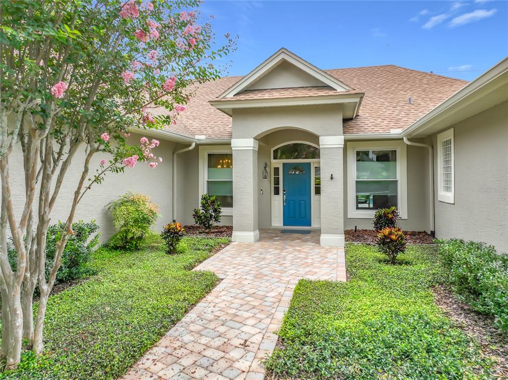 A beige house exterior features a blue front door, a brick walkway, and landscaping — 2667 COCHISE TRAIL, WINTER PARK, FL