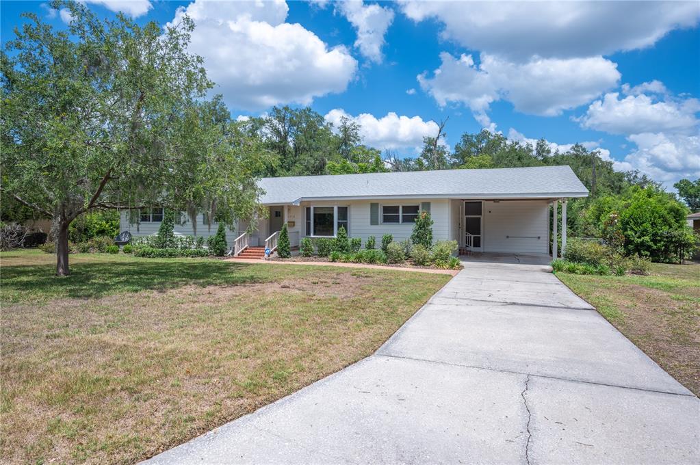 A single-story house with light siding, a concrete driveway, and a carport under a cloudy sky — 2718 BERKELEY AVENUE, LAKELAND, FL