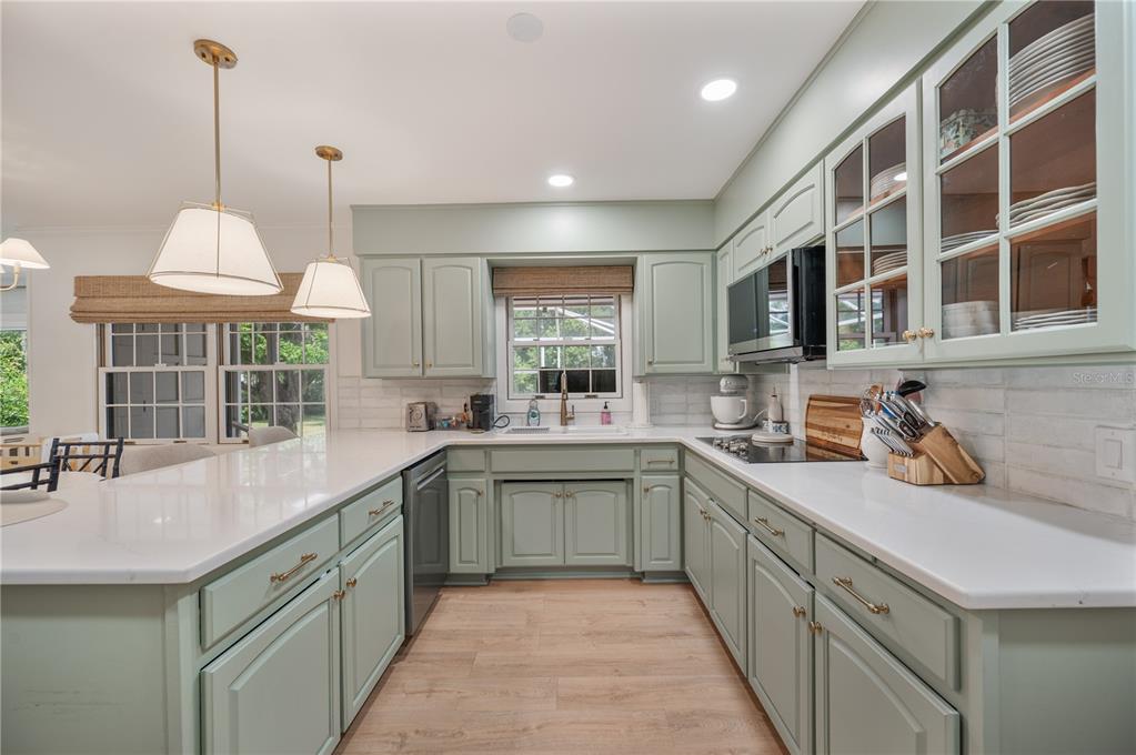 A kitchen features sage green cabinets, white countertops, a window, and two hanging pendant lights — 2718 BERKELEY AVENUE, LAKELAND, FL