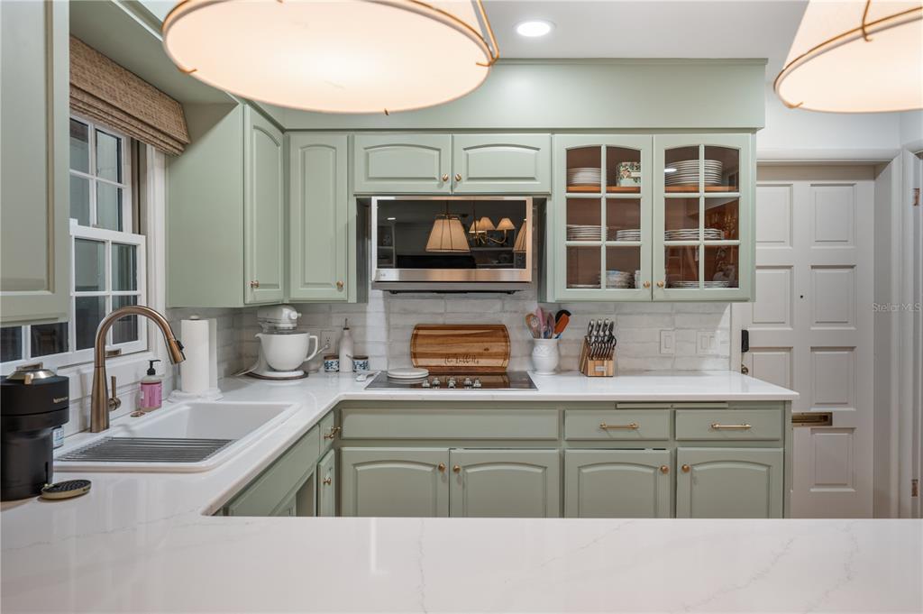 A kitchen features sage green cabinets, white countertops, a white farmhouse sink, and stainless appliances — 2718 BERKELEY AVENUE, LAKELAND, FL