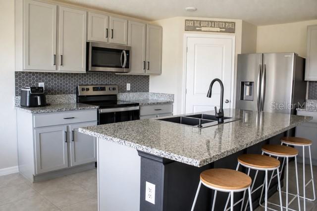 A modern kitchen features light gray cabinets, granite countertops, a center island, and stainless appliances — 4208 DOVETAIL LANE, PALMETTO, FL