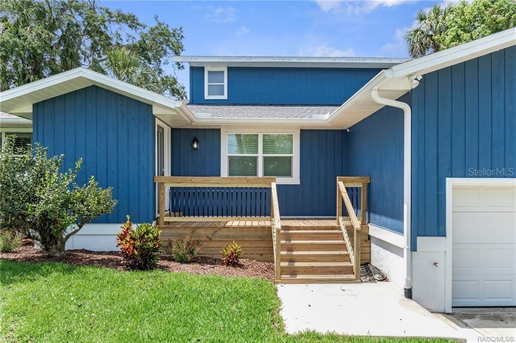 A blue house exterior features a wooden deck, stairs, and a white garage door — 9205 W HARBOR ISLE COURT, CRYSTAL RIVER, FL