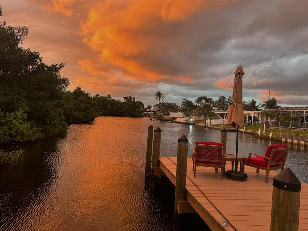 A wooden dock with two chairs and an umbrella overlooks a canal at sunset — 265 96TH AVENUE N, ST PETERSBURG, FL
