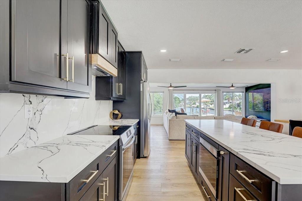 A modern kitchen with dark cabinets, white marble countertops, and a view of a living area — 265 96TH AVENUE N, ST PETERSBURG, FL