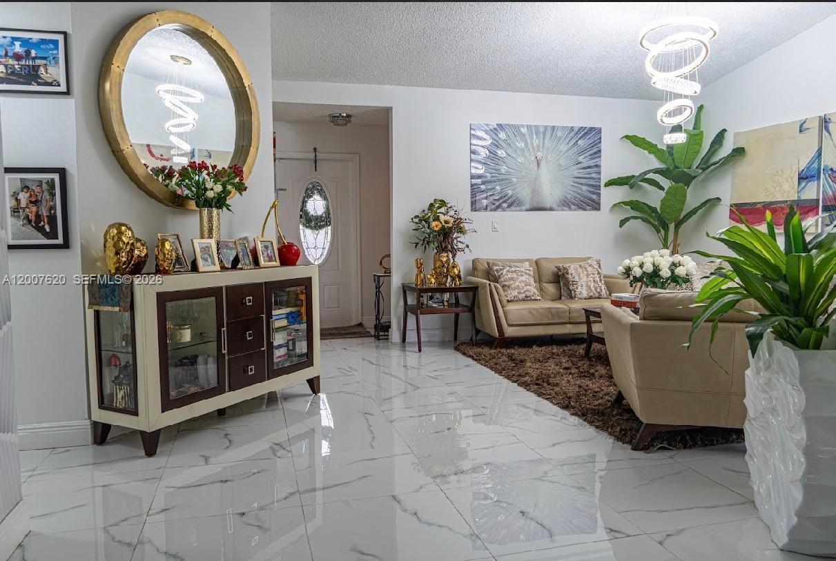 A living room features white marble flooring, beige sofas, a large round mirror, and decor — 8419 NW 193rd Ln, Hialeah FL 33015, HIALEAH, FL
