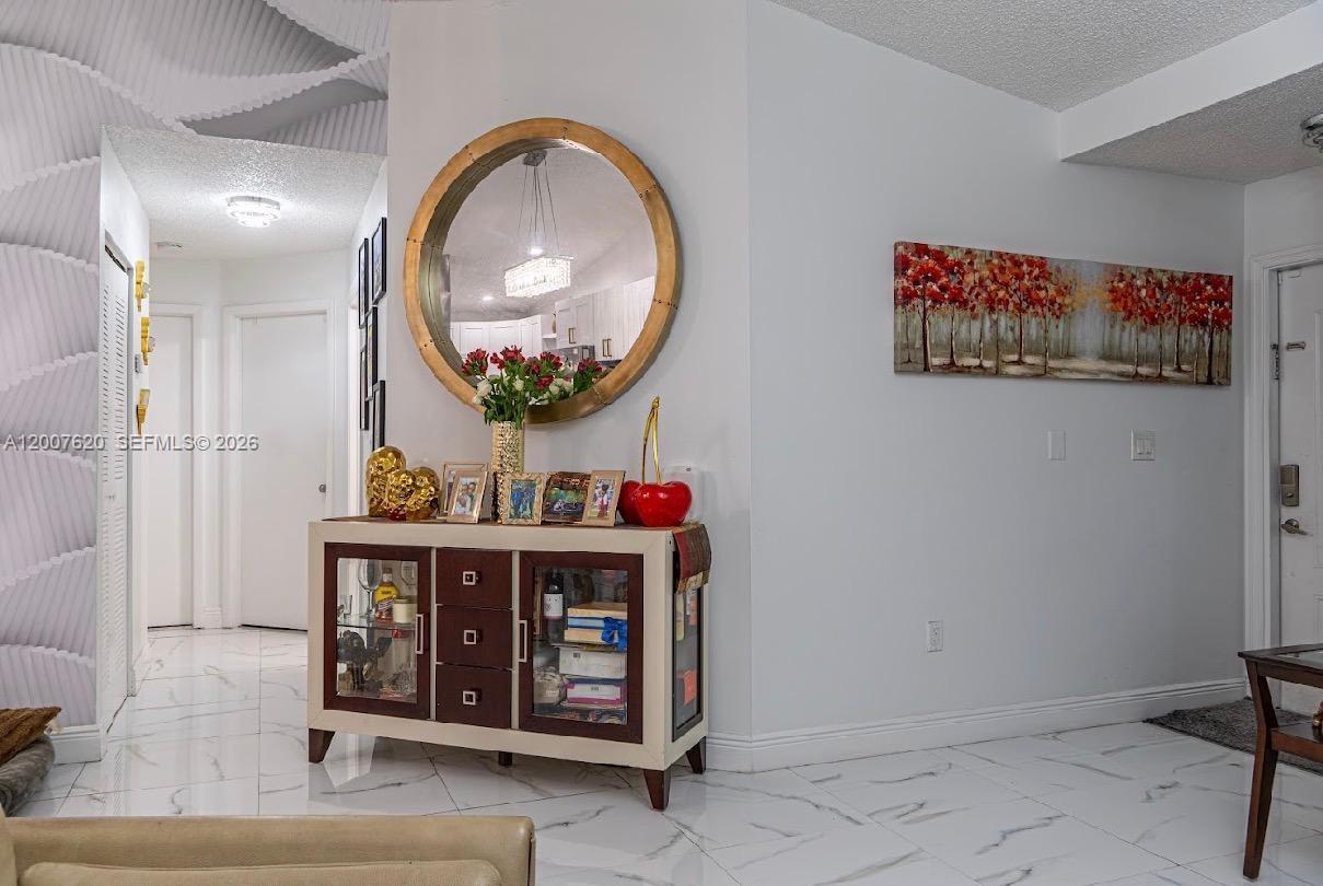 A white-walled entryway features a round mirror, a wooden console table, and tile flooring — 8419 NW 193rd Ln, Hialeah FL 33015, HIALEAH, FL