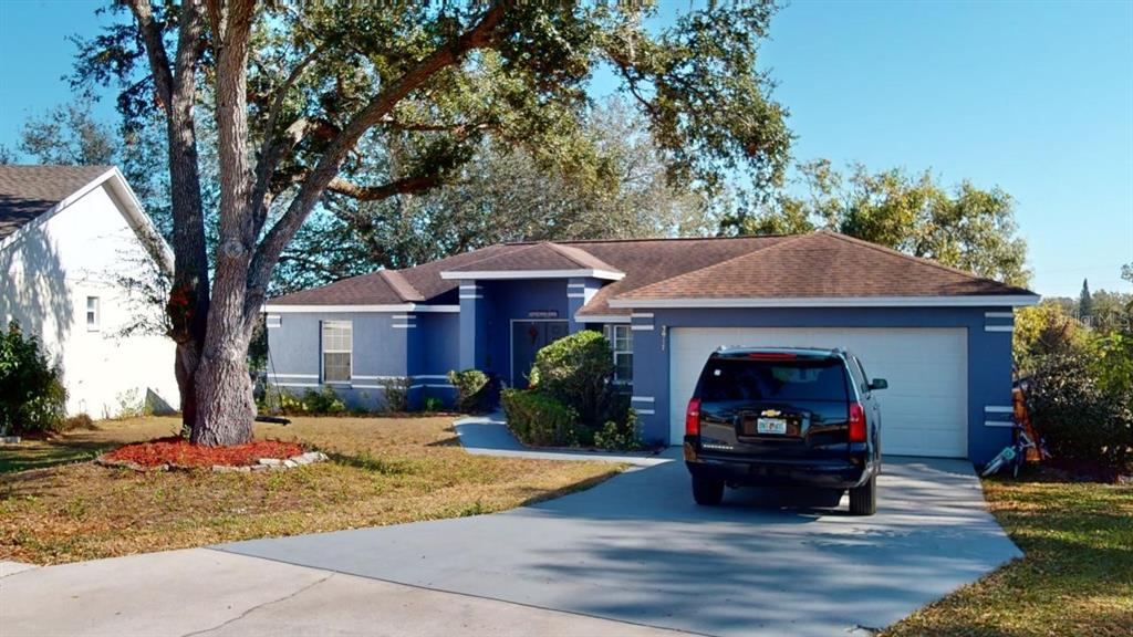 A blue single-story house with a two-car garage and a large tree in the yard — 3917 DERBY DRIVE, LAKELAND, FL
