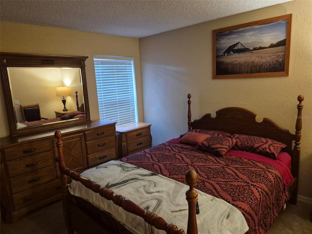 A bedroom features a wooden bed frame, a matching dresser with a mirror, and wall art — 5124 CONROY ROAD UNIT 11, ORLANDO, FL