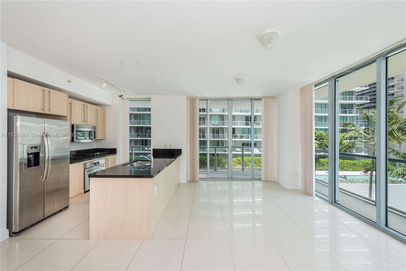 A modern kitchen with light wood cabinets, black countertops, and large windows overlooking a pool — 79 SW 12th St, Miami FL 33130, MIAMI, FL