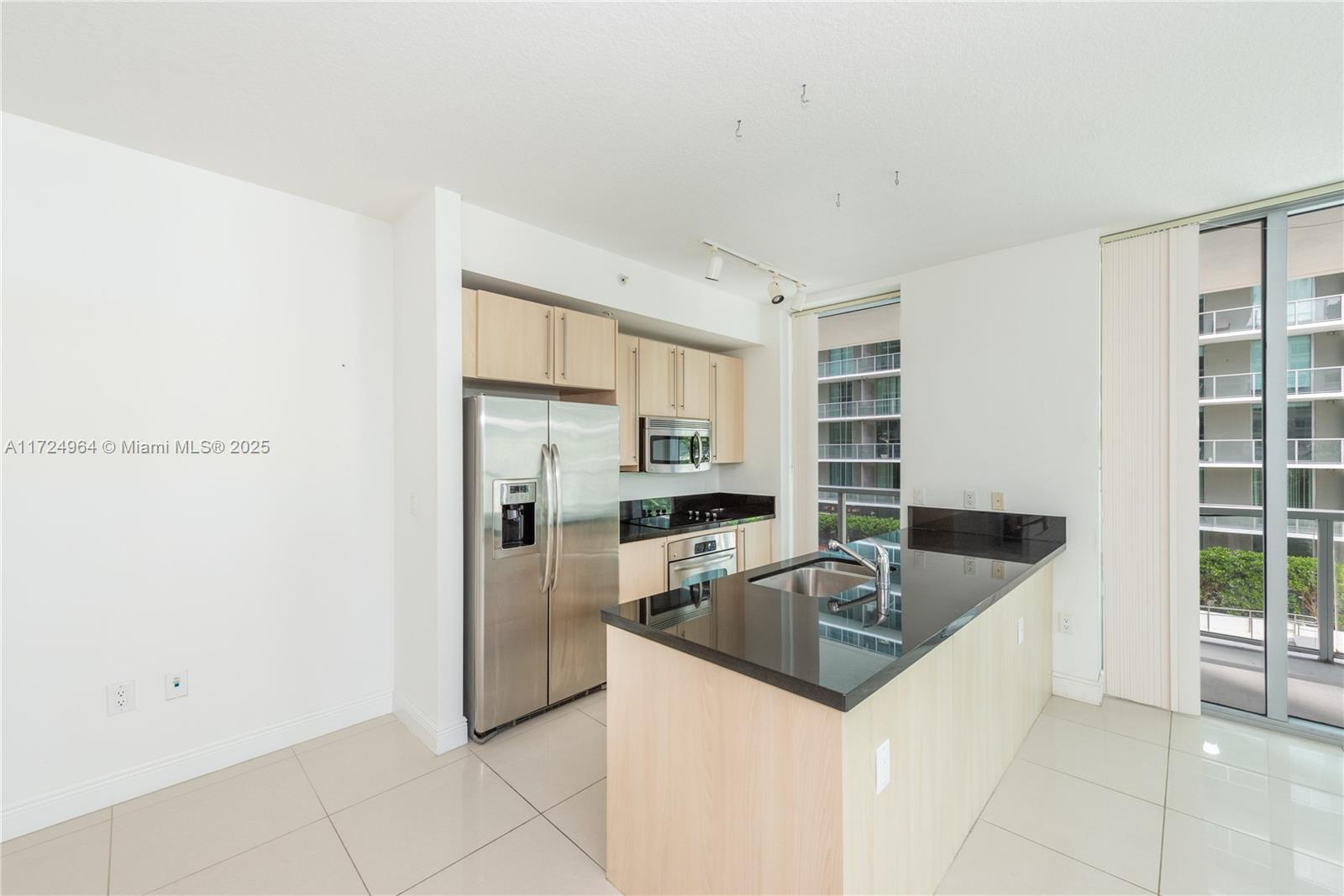 A modern kitchen features light wood cabinets, black countertops, stainless steel appliances, and tile flooring — 79 SW 12th St, Miami FL 33130, MIAMI, FL