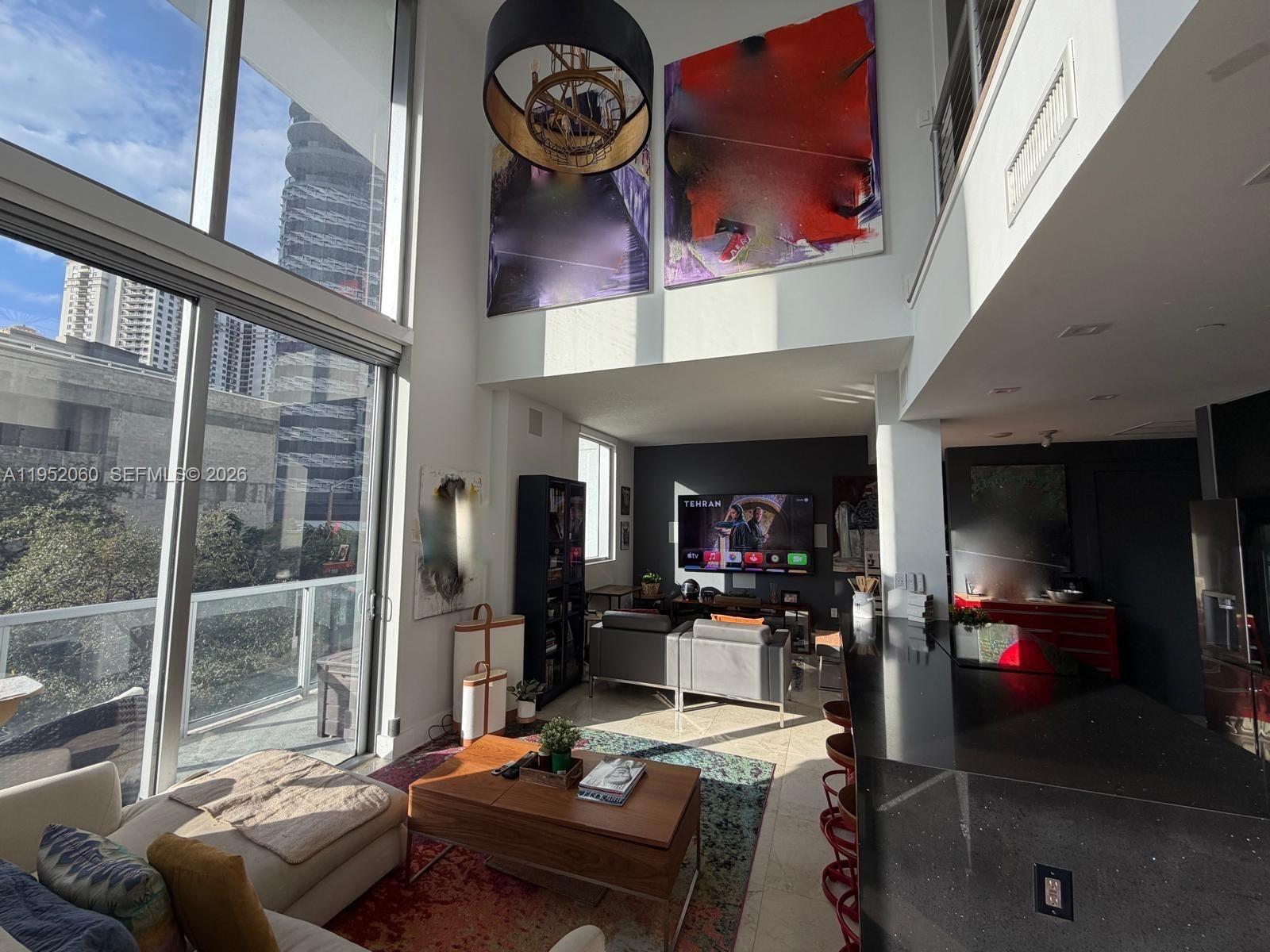 A modern, two-story living room features floor-to-ceiling windows, large abstract wall art, and a kitchen — 1050 Brickell Ave # 222, Miami FL 33131, MIAMI, FL