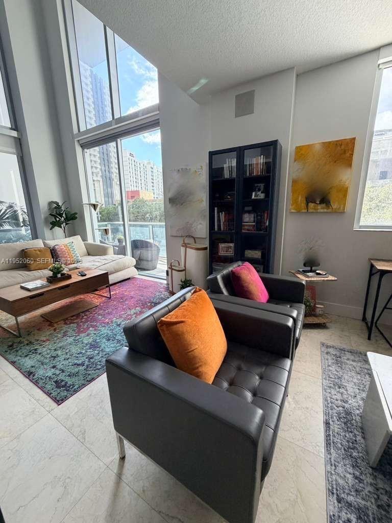 A modern living room features high ceilings, floor-to-ceiling windows, and contemporary furniture on tiled floors — 1050 Brickell Ave # 222, Miami FL 33131, MIAMI, FL