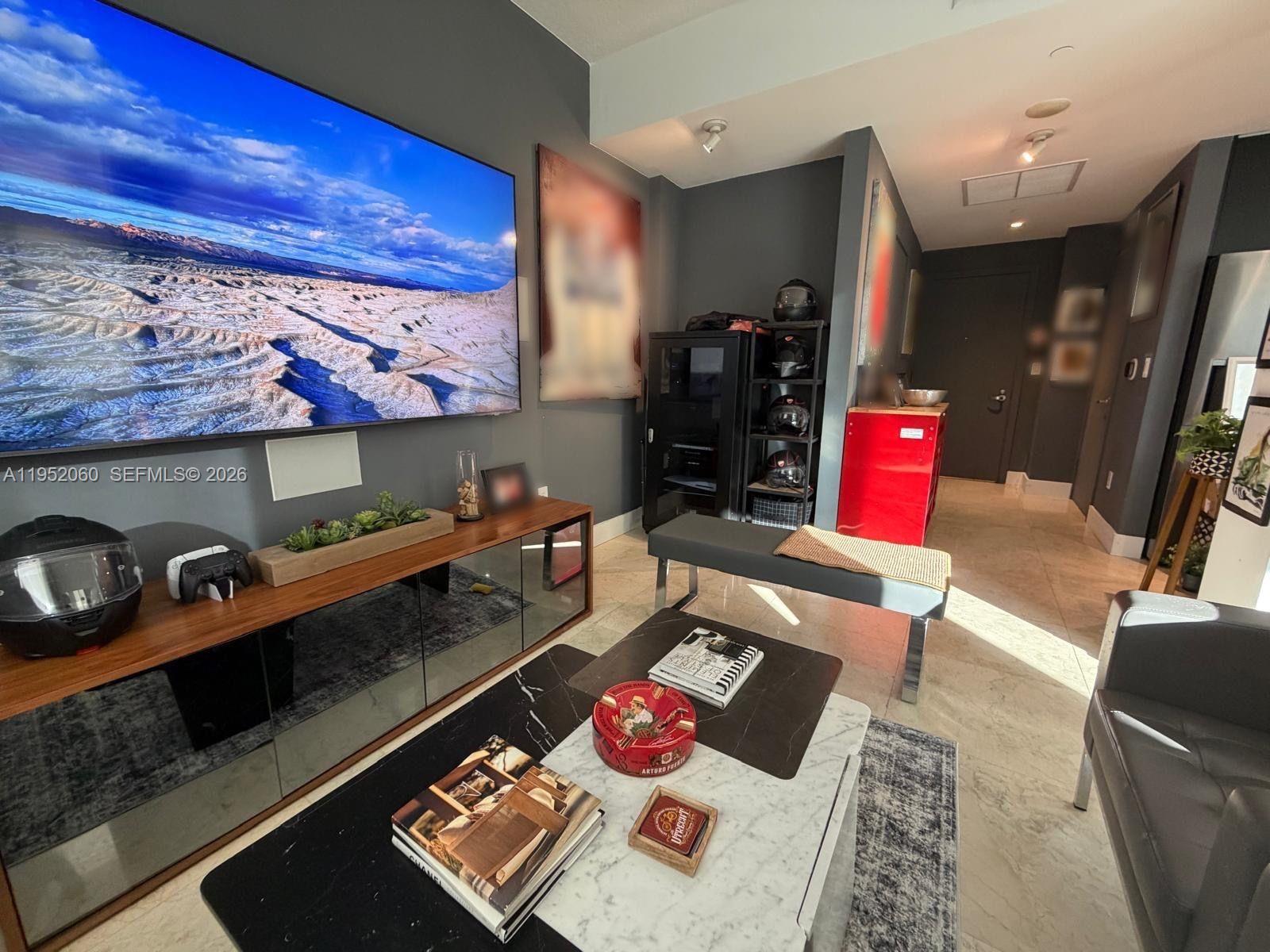 A modern living room features a large wall-mounted television, a marble coffee table, and dark walls — 1050 Brickell Ave # 222, Miami FL 33131, MIAMI, FL