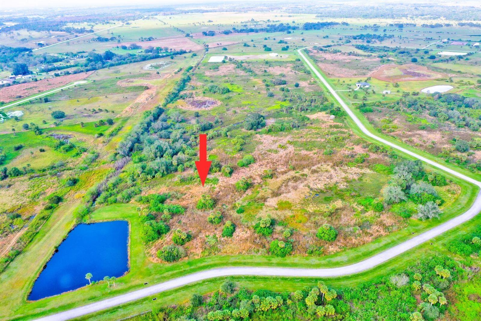 An aerial view shows a large, undeveloped grassy lot with scattered trees and a pond — 2831 SE 67th Place, Okeechobee FL 34974, OKEECHOBEE, FL