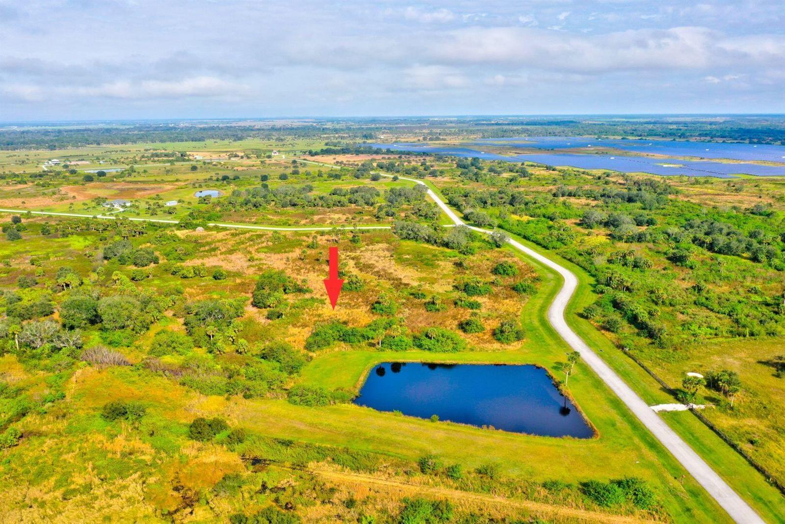 An aerial view shows a red arrow pointing to a vacant lot near a pond — 2831 SE 67th Place, Okeechobee FL 34974, OKEECHOBEE, FL