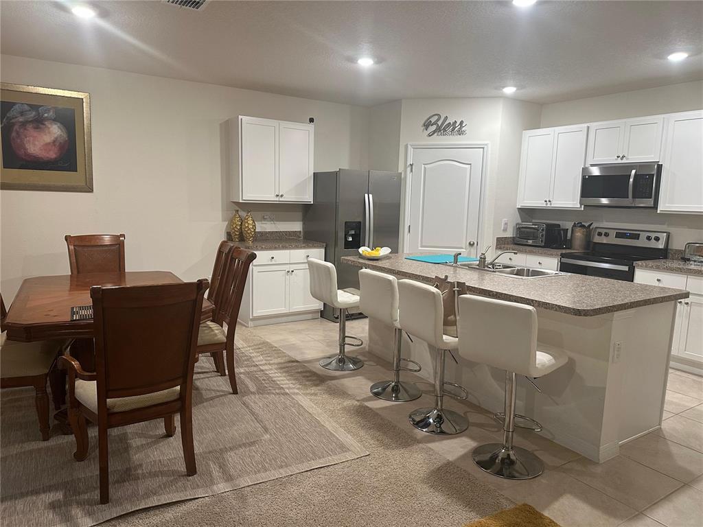 A kitchen with white cabinets, stainless steel appliances, and an island with three bar stools — 303 ALENCON WAY, KISSIMMEE, FL