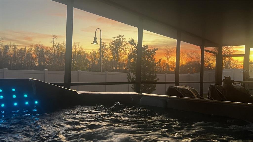 A hot tub with glowing blue lights sits on a screened-in porch at sunset — 4382 FINCH LANE, KISSIMMEE, FL
