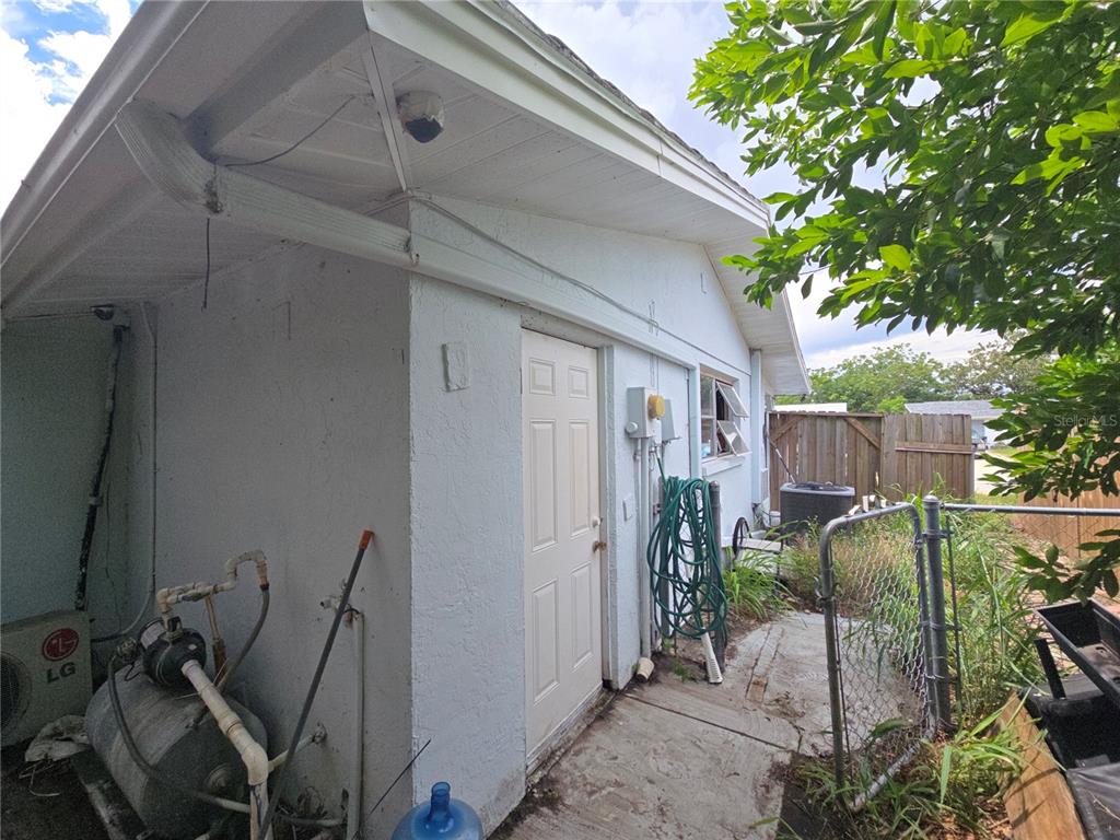 An exterior view of a white house with a water pump, hose, and chain-link fence — 7809 WAXWOOD DRIVE, PORT RICHEY, FL