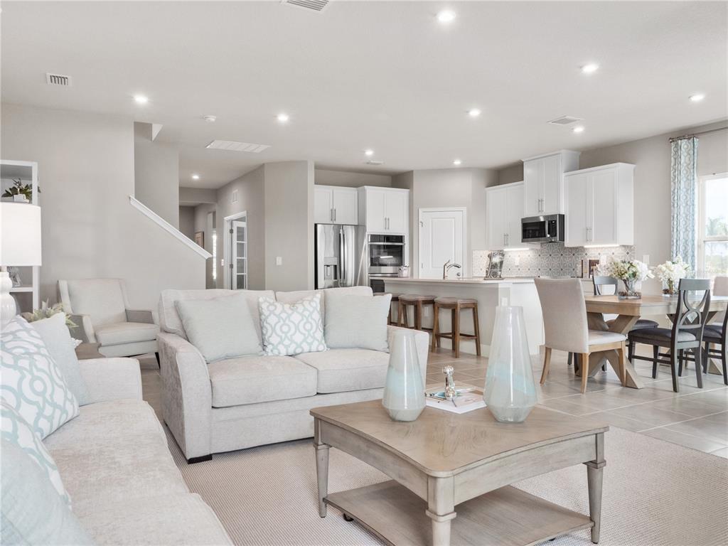 An open-concept living room and kitchen feature white cabinetry, light-toned furniture, and tile flooring — 6040 RIVERFRONT WAY, ST CLOUD, FL