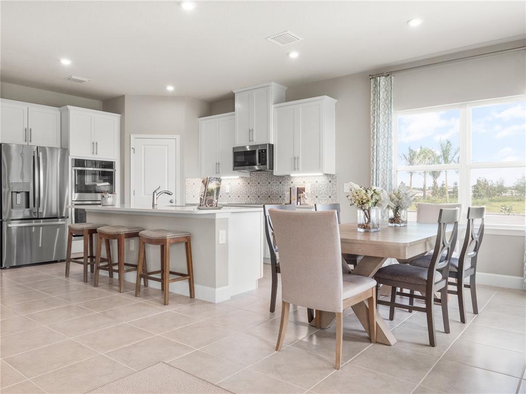 A kitchen with white cabinets, stainless steel appliances, and an island next to a dining area — 6040 RIVERFRONT WAY, ST CLOUD, FL