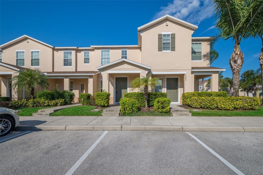 A two-story townhouse exterior with a beige stucco facade, green shutters, and a palm tree — 5087 DOMINICA DRIVE, KISSIMMEE, FL