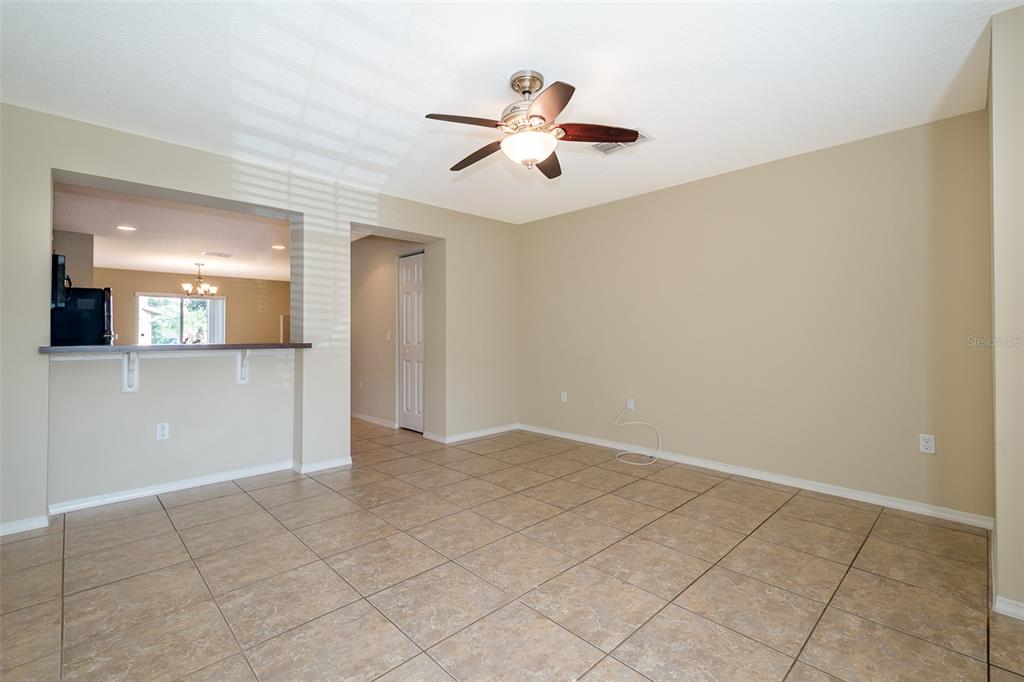 An empty living room features beige walls, a ceiling fan, and light-colored tile flooring — 5087 DOMINICA DRIVE, KISSIMMEE, FL