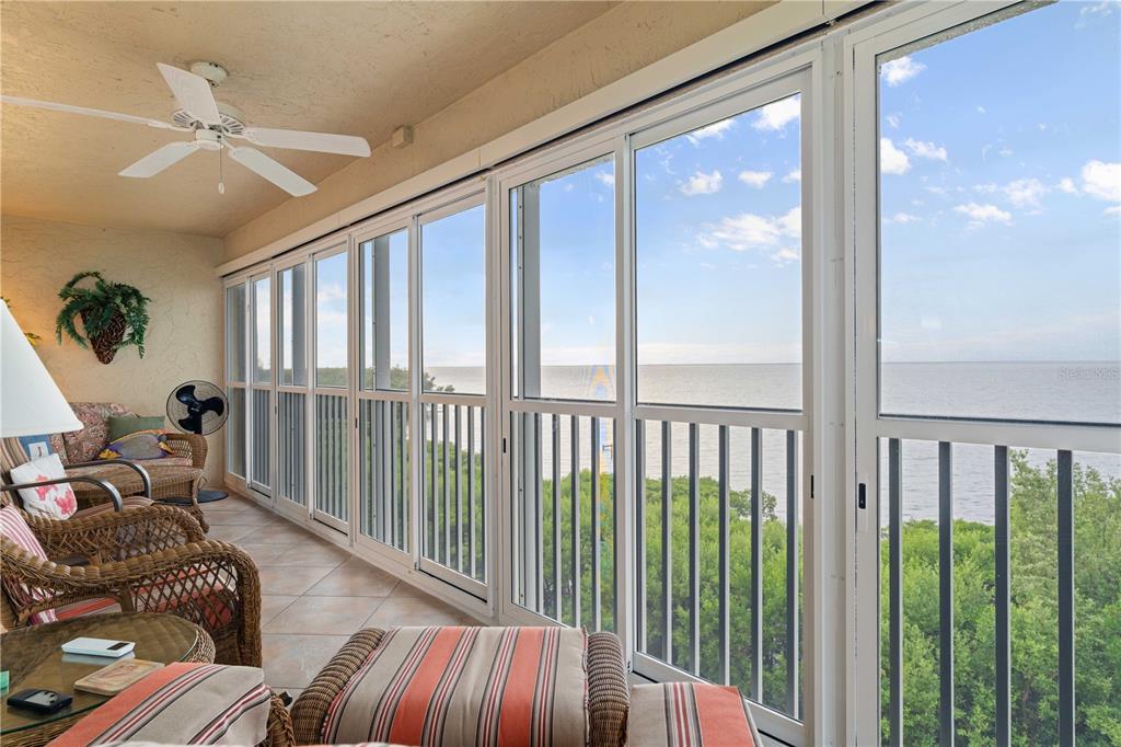 A sunroom features wicker furniture, a ceiling fan, and sliding glass doors overlooking the ocean — 101 N MARION COURT UNIT 235, PUNTA GORDA, FL