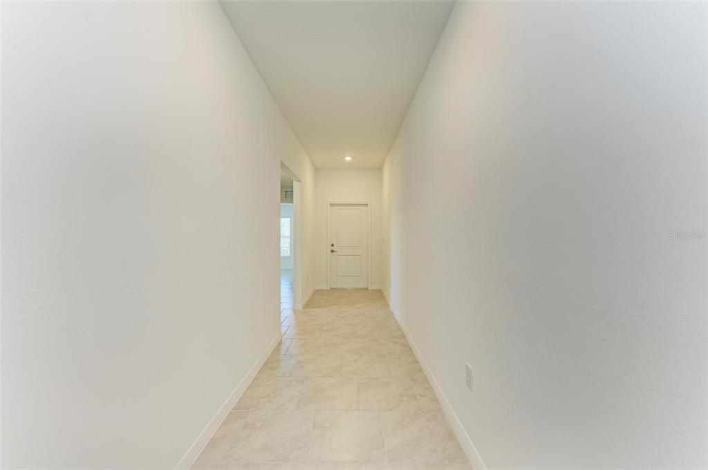 A long, narrow hallway with light-colored tile flooring leads to a closed white door — 23444 STEEPLE AVENUE, PUNTA GORDA, FL