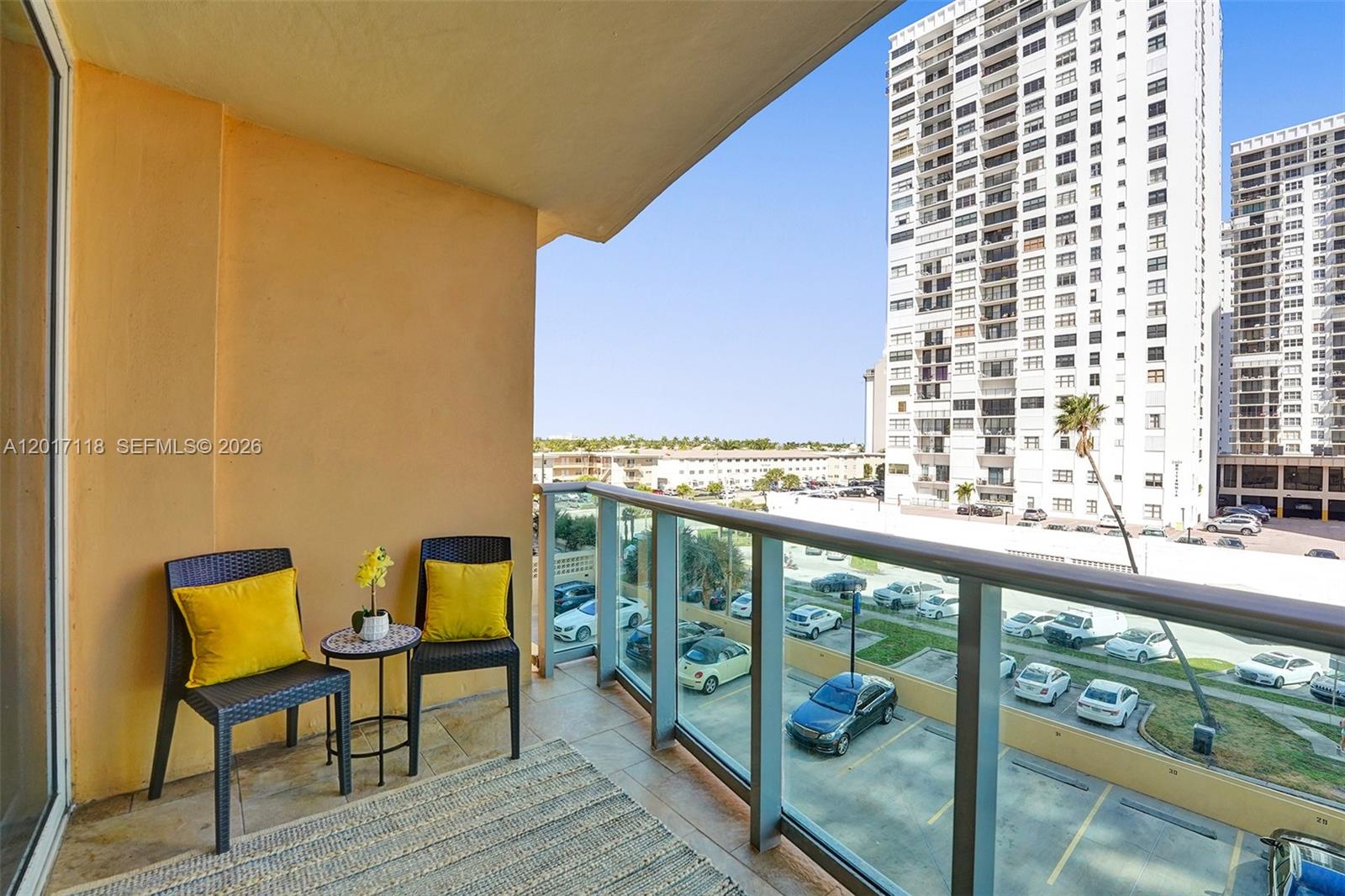 A balcony with two chairs, a small table, and a glass railing overlooks a parking lot — 2501 S Ocean Dr, Hollywood FL 33019, HOLLYWOOD, FL