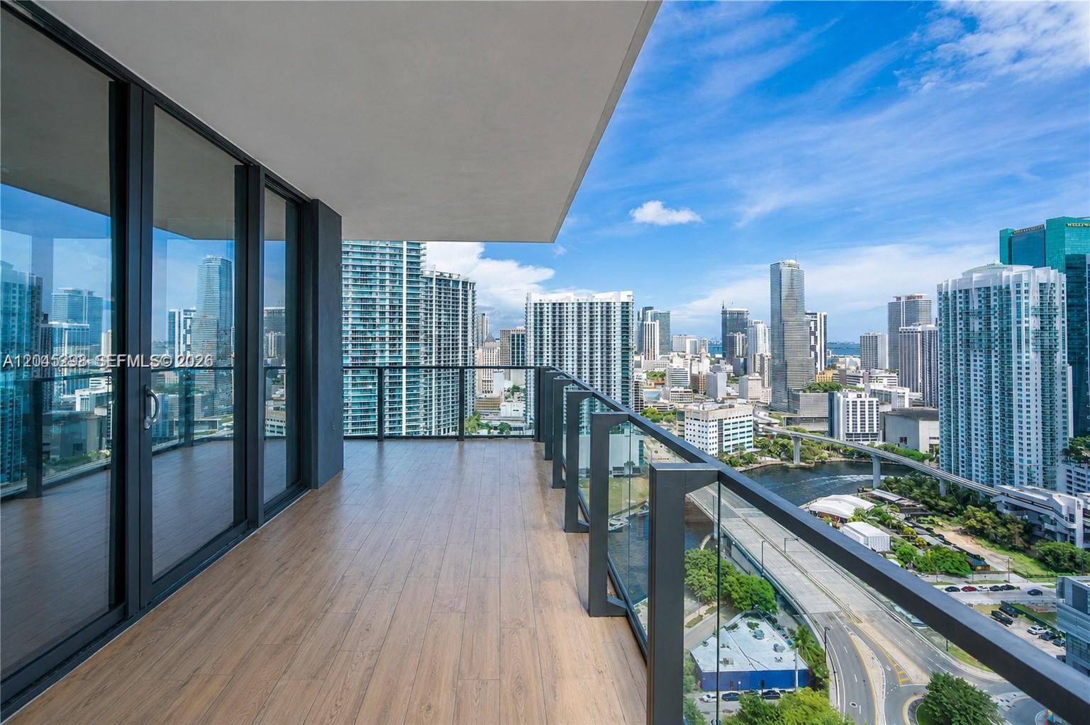 A high-rise balcony with wood-look flooring overlooks a dense urban cityscape and a river — 88 SW 7th St # 1511, Miami FL 33130, MIAMI, FL