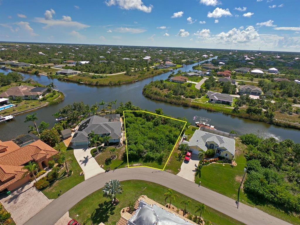 An aerial view shows a vacant, tree-covered residential lot situated between two houses along a canal — 9604 ARNAZ CIRCLE, PORT CHARLOTTE, FL