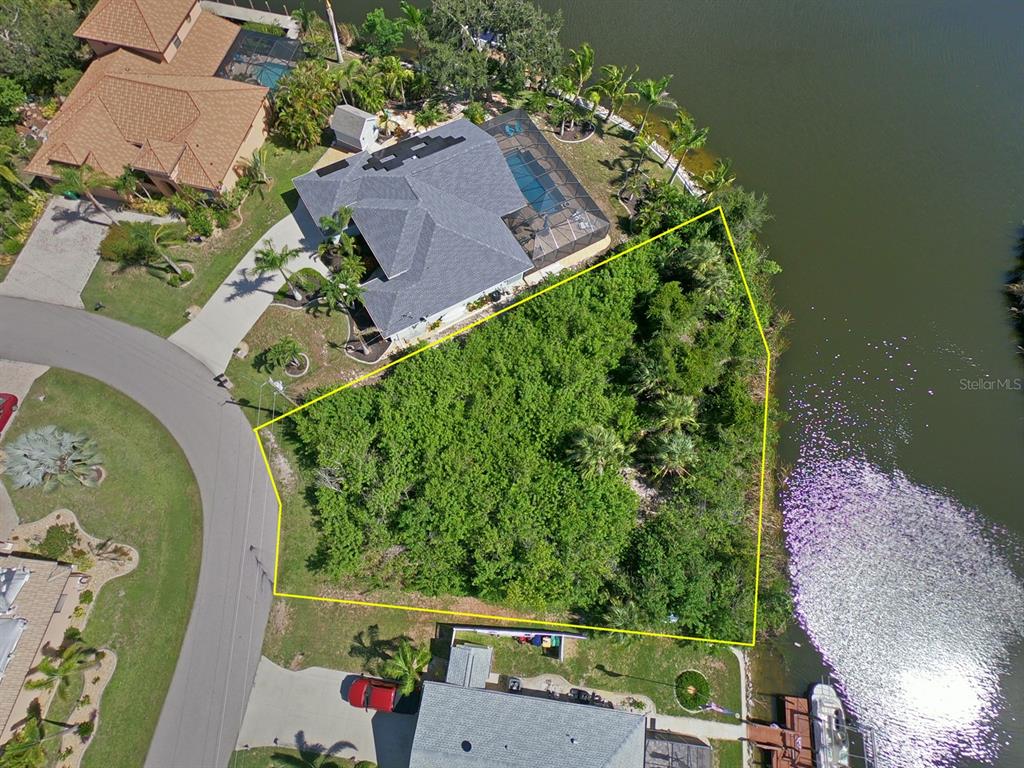 An aerial view shows a vacant, wooded waterfront lot outlined in yellow next to houses — 9604 ARNAZ CIRCLE, PORT CHARLOTTE, FL