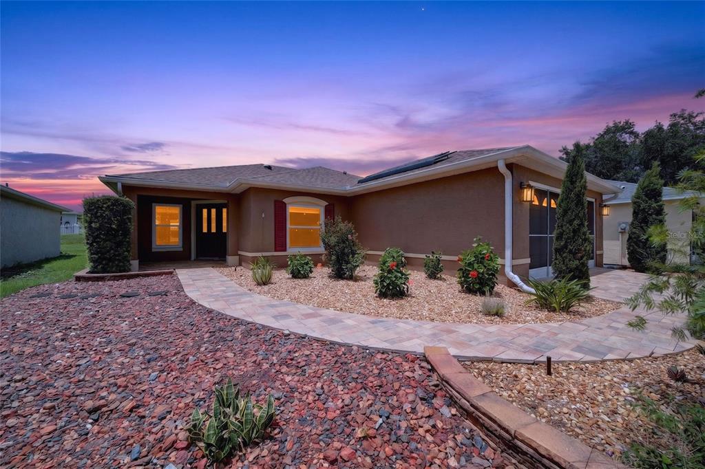 A single-story house with a tan stucco exterior, a paved walkway, and a gravel yard — 9702 SW 92ND PLACE ROAD, OCALA, FL