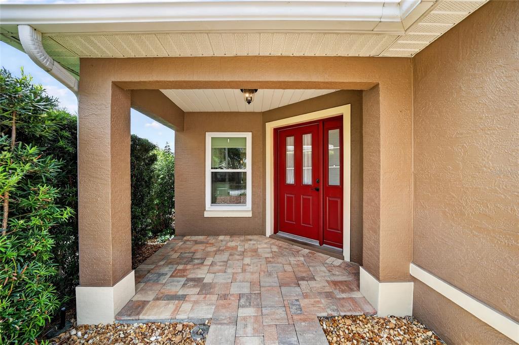 A covered entryway features a red front door, a window, and stone paver flooring — 9702 SW 92ND PLACE ROAD, OCALA, FL